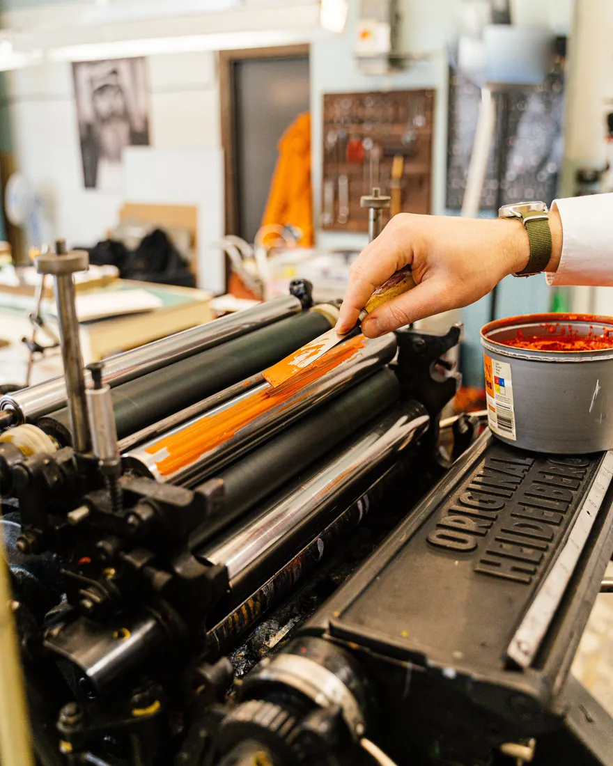 Mano aplicando tinta sobre los rodillos de una prensa tipográfica